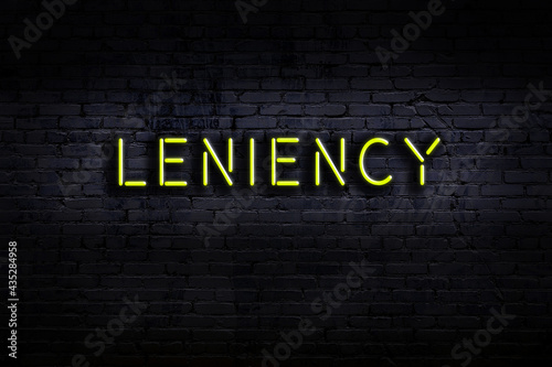 Neon sign. Word leniency against brick wall. Night view