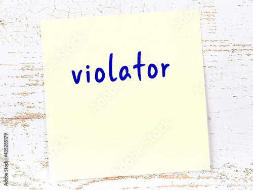 Yellow sticky note on wooden wall with handwritten word violator photo