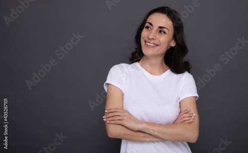 Young beautiful stylish happy woman in a white t-shirt is posing on the gray background