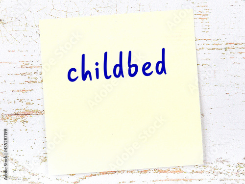 Yellow sticky note on wooden wall with handwritten word childbed