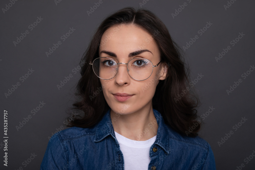 Close up portrait of a confident attractive young brunette woman in eyeglasse on gray wall background Close up portrait of a confident attractive young brunette woman in eyeglasse on gray wall background