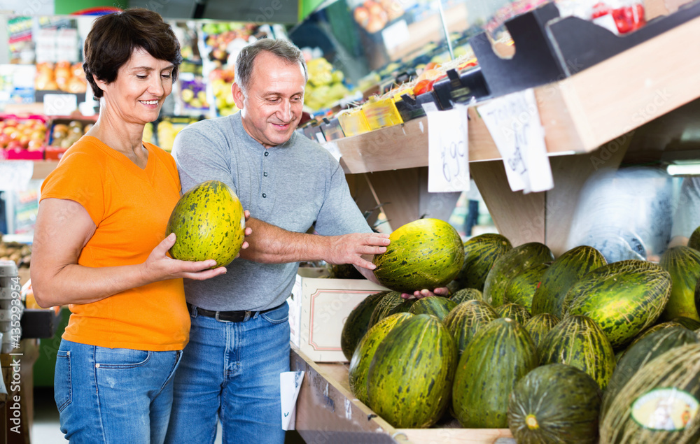 Fototapeta premium Smiling glad couple is choosing green melon in the supermarket.
