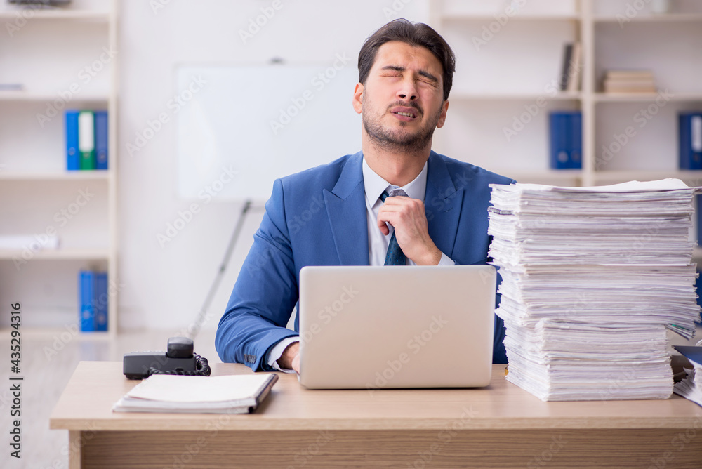 Young male employee unhappy with excessive work in the office Young male employee unhappy with excessive work in the office