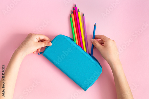 Obraz na plátně Rainbow multicolored pencils in a blue pencil case in the hands of a child on a pink background