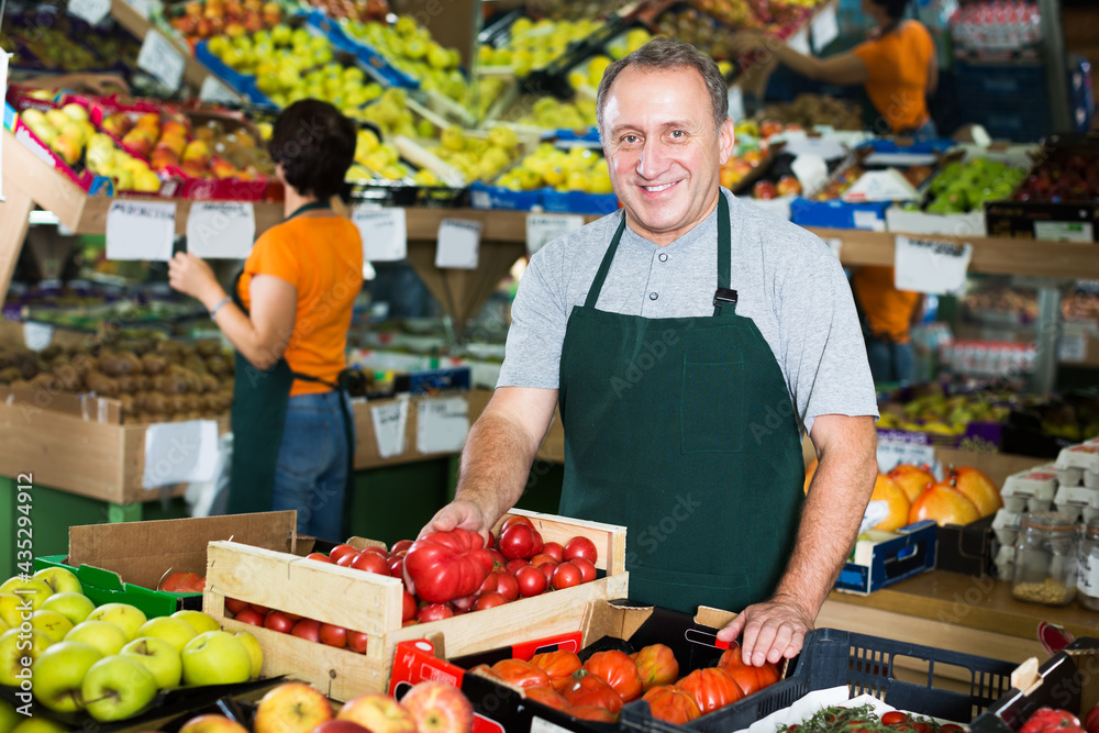 Obraz premium positive adult seller is offering red tomatos in the market.