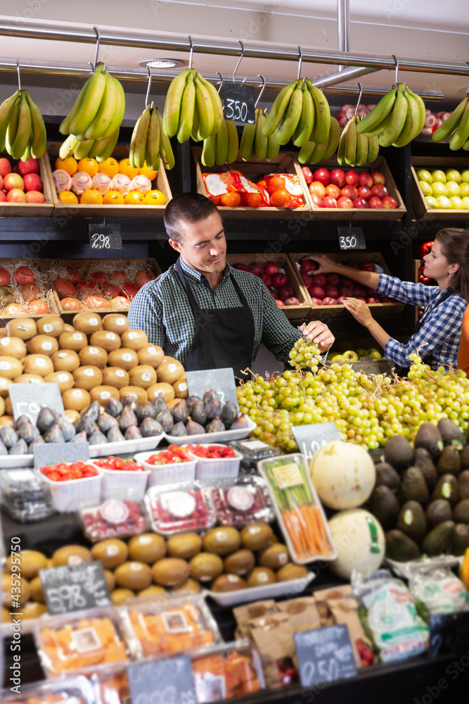 Male and female sellers laying out fruits and vegetables behind the counter