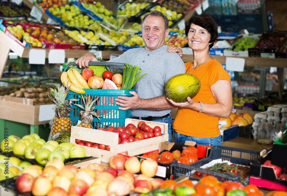 Family couple is standing with basket with vegetables and fruits in food store