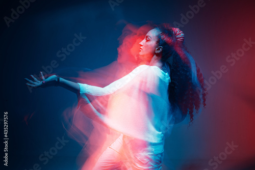 Fototapeta Naklejka Na Ścianę i Meble -  Colourful portrait of young mixed race girl dancing in studio. Long exposure. Colored neon light.