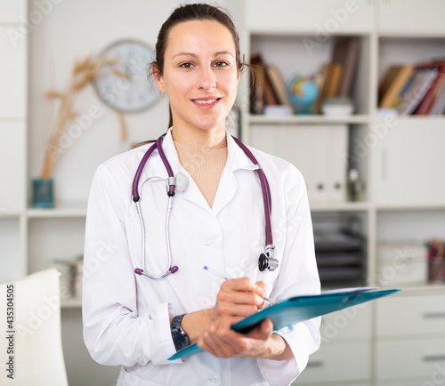 Positive woman doctor in formal wear standing with folder in office