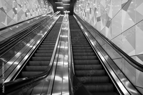 Selective focus and low angle view, black and white tone, interior view of stairway over handrail of escalator from underground metro station without people.