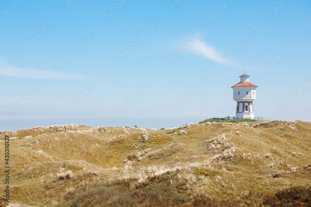 White water tower on a North Sea island with green dunes. Landscape on a German or Dutch island. Vacation on the North Sea	