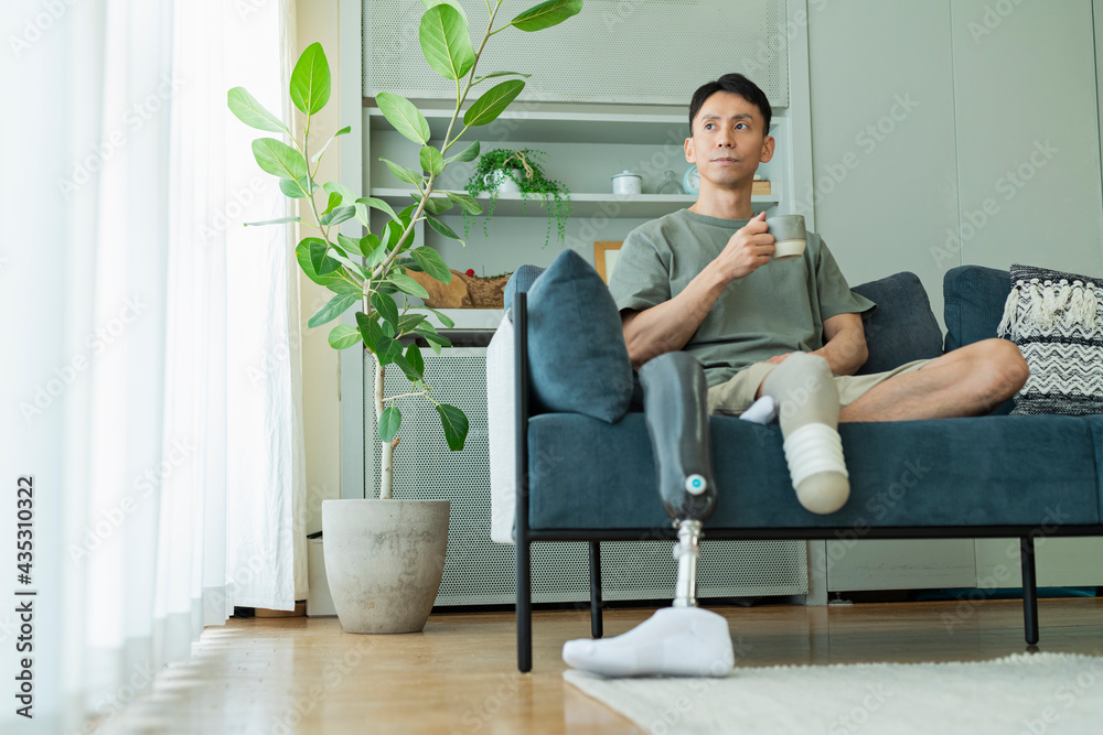 ソファでコーヒーを飲む義足の男性 ソファでコーヒーを飲む義足の男性