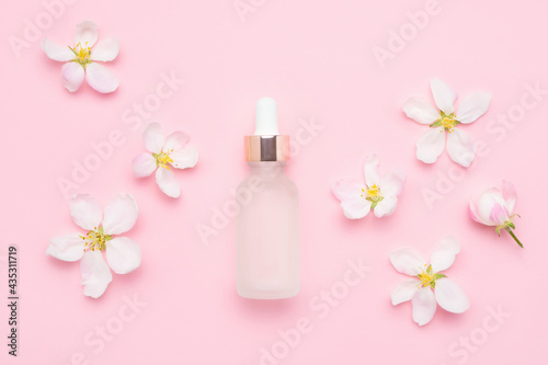Glass dropper bottle for medical and cosmetic use and apple tree blossom flowers on a pink background. SPA concept.