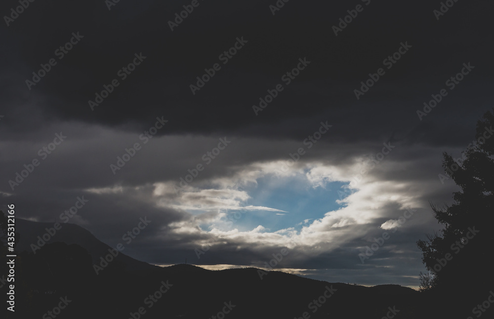 dark moody stormy sky with clouds opening up and letting sun rays and sunbeam shining through