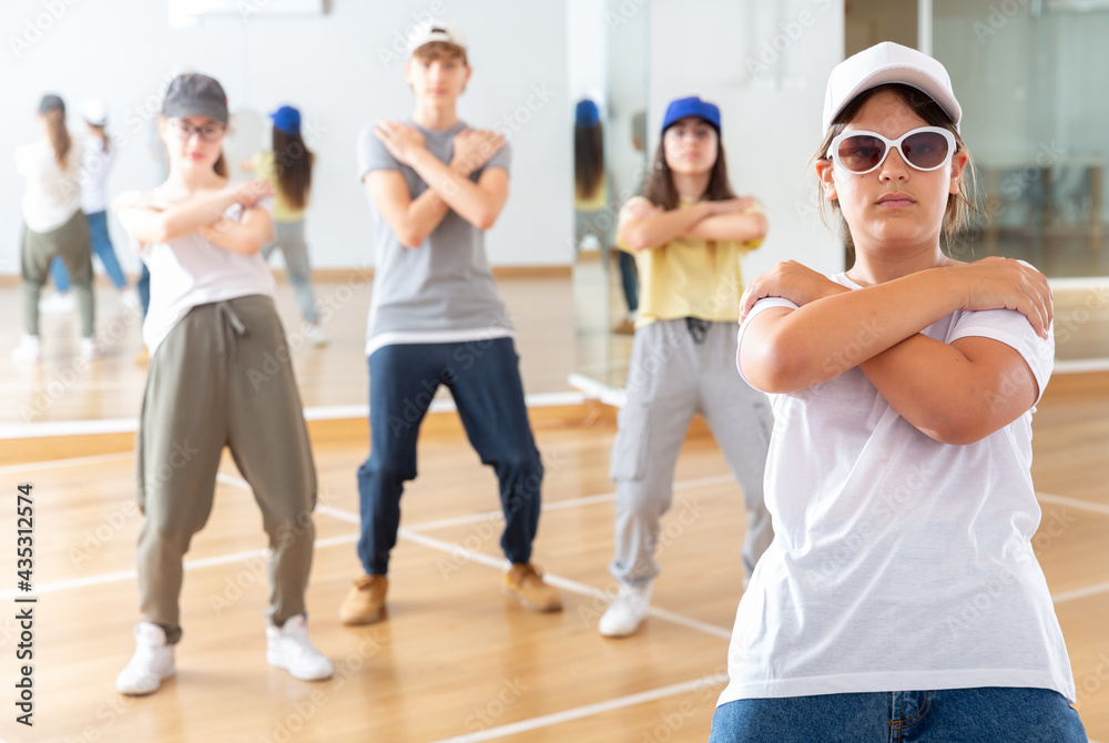Portrait of emotional teenager girl doing hip hop movements during group class in dance studio