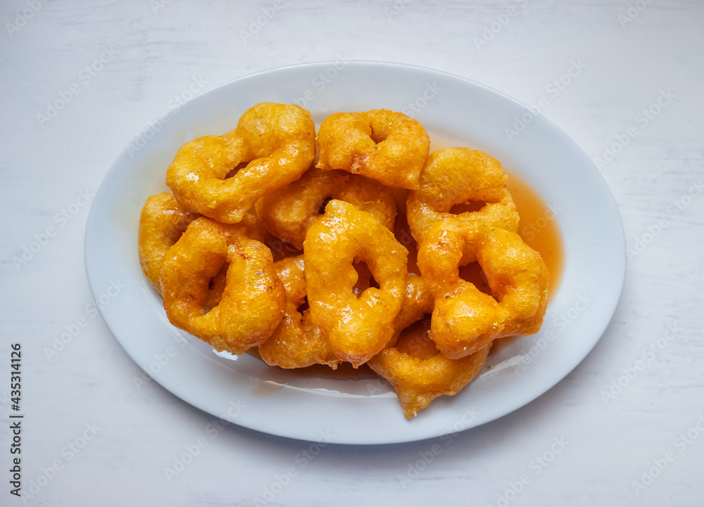 Picarones, Peruvian Dessert made from Squash and Sweet Potato and Served in a Doughnut Form with Syrup made from Panela on a White Table