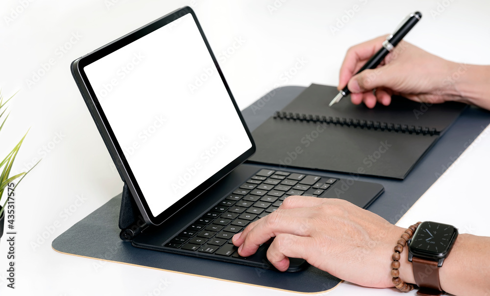 Cropped shot of man hands working on tablet keyboard and writing on notebook while sitting at the table. Cropped shot of man hands working on tablet keyboard and writing on notebook while sitting at the table.