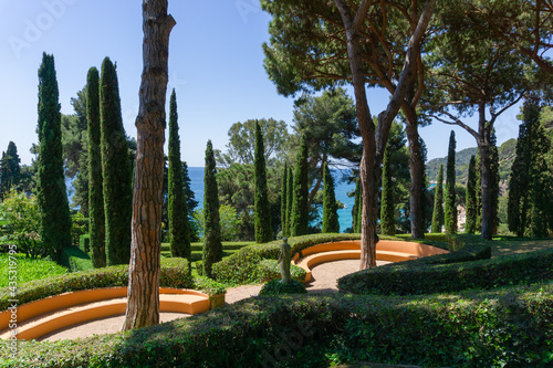 Orange stone benches between trees and plants in a garden overlooking the Mediterranean Sea