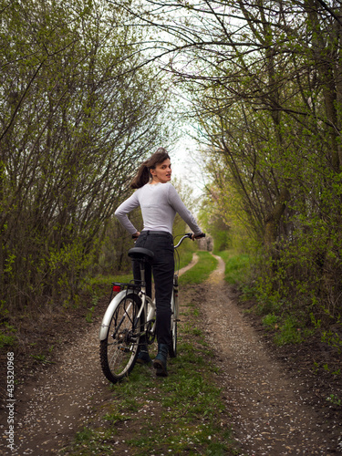 A woman with a bicycle on a country road under flowering trees.