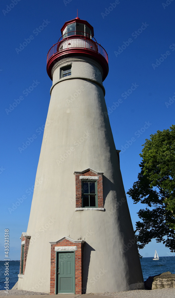 the historic and picturesque  marblehead lighthouse and a sailboat on a sunny day in summer on lake erie,  near sandusky, ohio