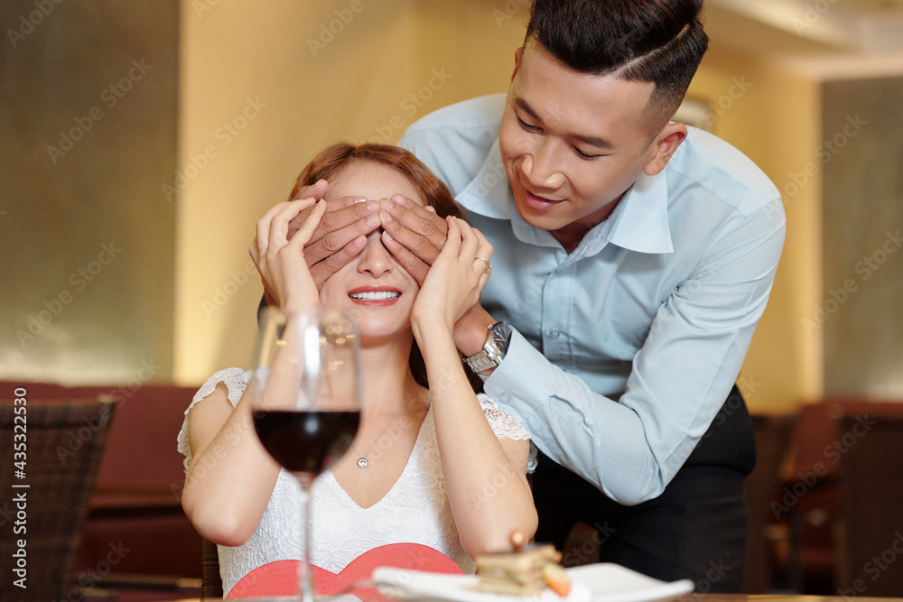 Handsome young man covering eyes of girlfriend after bringing her delicious dessert as surprise Handsome young man covering eyes of girlfriend after bringing her delicious dessert as surprise