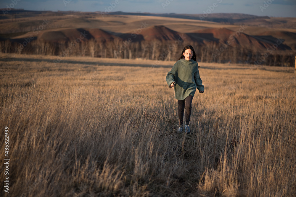 Little girl runs away into the open air field. Happy and having fun. Beautiful landscape, sunset, golden light.