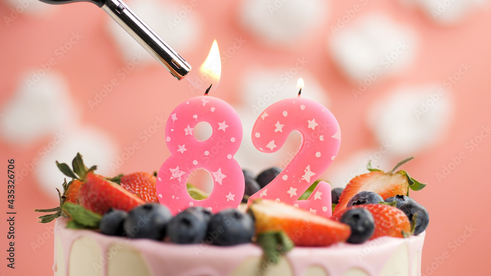 Birthday cake number 82, pink candle on beautiful cake with berries and  lighter with fire against background of white clouds and pink sky. Close-up  Stock Photo | Adobe Stock