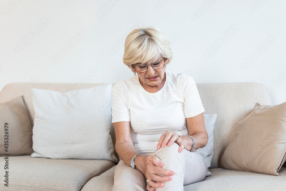 Senior woman holding the knee with pain. Old age, health problem and people concept - senior woman suffering from pain in leg at home. Elderly woman suffering from pain in knee at home Senior woman holding the knee with pain. Old age, health problem and people concept - senior woman suffering from pain in leg at home. Elderly woman suffering from pain in knee at home