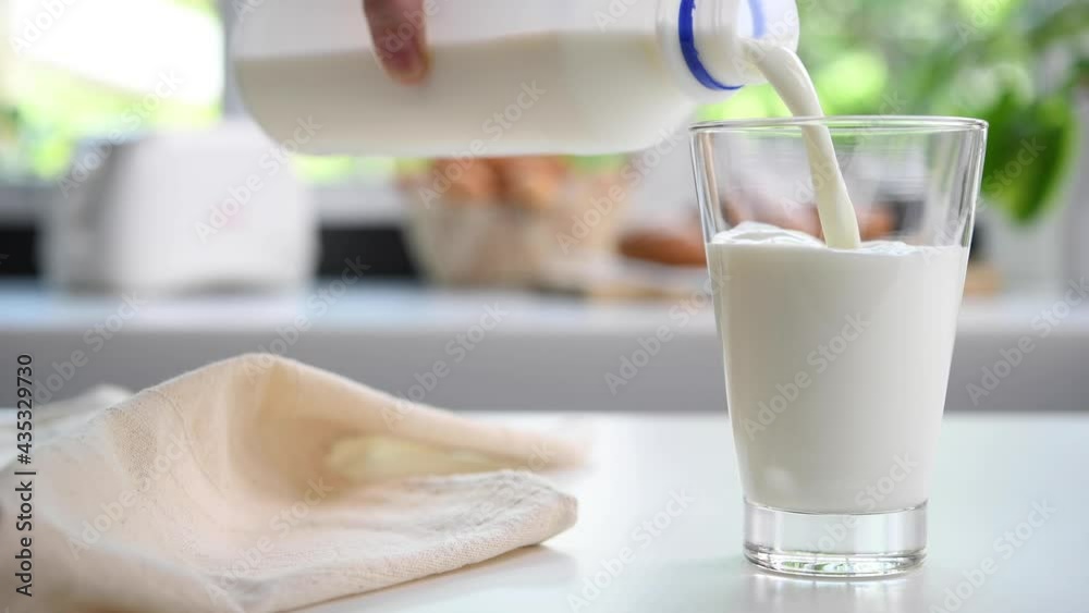 Pouring milk from plastic bottle into a glass in the kitchen