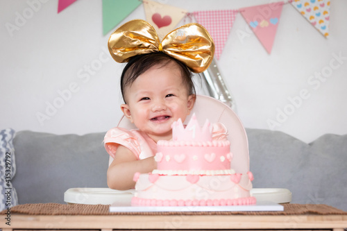 Portrait of cute asian baby girl celebrating her first birthday with pink princess cake with happiness. photo