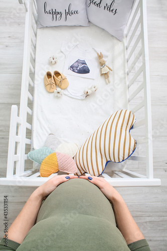 Pregnant woman near crib wi...
