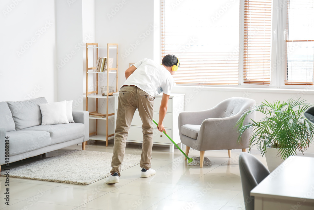 Young man listening to music while mopping floor in living room