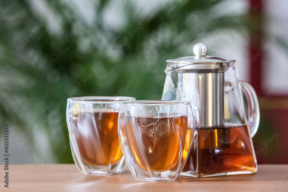 Teapot and glasses with hot tea on table in room Teapot and glasses with hot tea on table in room