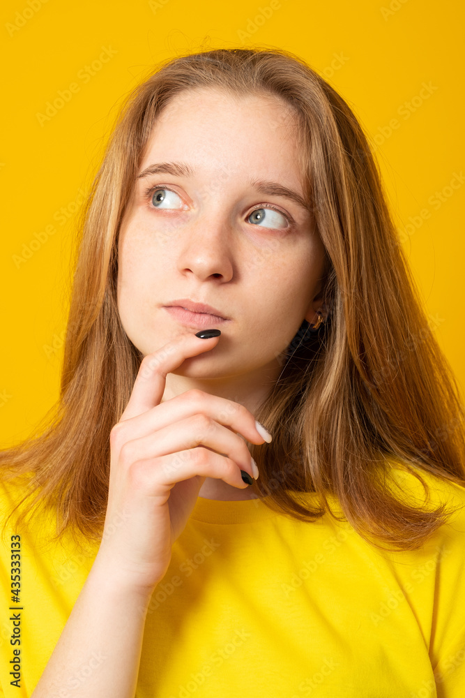 Pleasant looking teen girl holds chin and looks pensive away, thinks about great plan, has new ideas in mind, wears bright yellow t shirt. Pleasant looking teen girl holds chin and looks pensive away, thinks about great plan, has new ideas in mind, wears bright yellow t shirt.