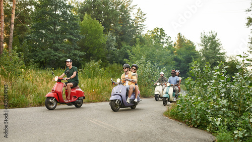 Happy young multiracial friends riding retro scooters