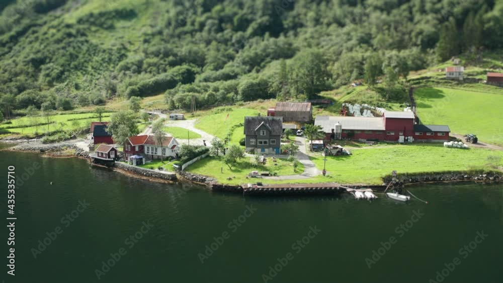 A farm on the shore of the Naeroyfjord. Green pasture stretching from the waterline to the hills. A herd of sheep grazing on the meadow. Forest covering mountain foothills. A farm on the shore of the Naeroyfjord. Green pasture stretching from the waterline to the hills. A herd of sheep grazing on the meadow. Forest covering mountain foothills.