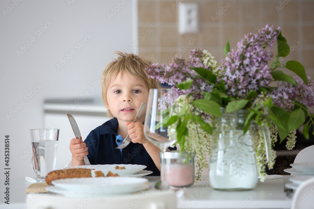 Close portrait of a beautiful blond child, toddler boy with vase with lilacs at home, sitting on the table Close portrait of a beautiful blond child, toddler boy with vase with lilacs at home, sitting on the table