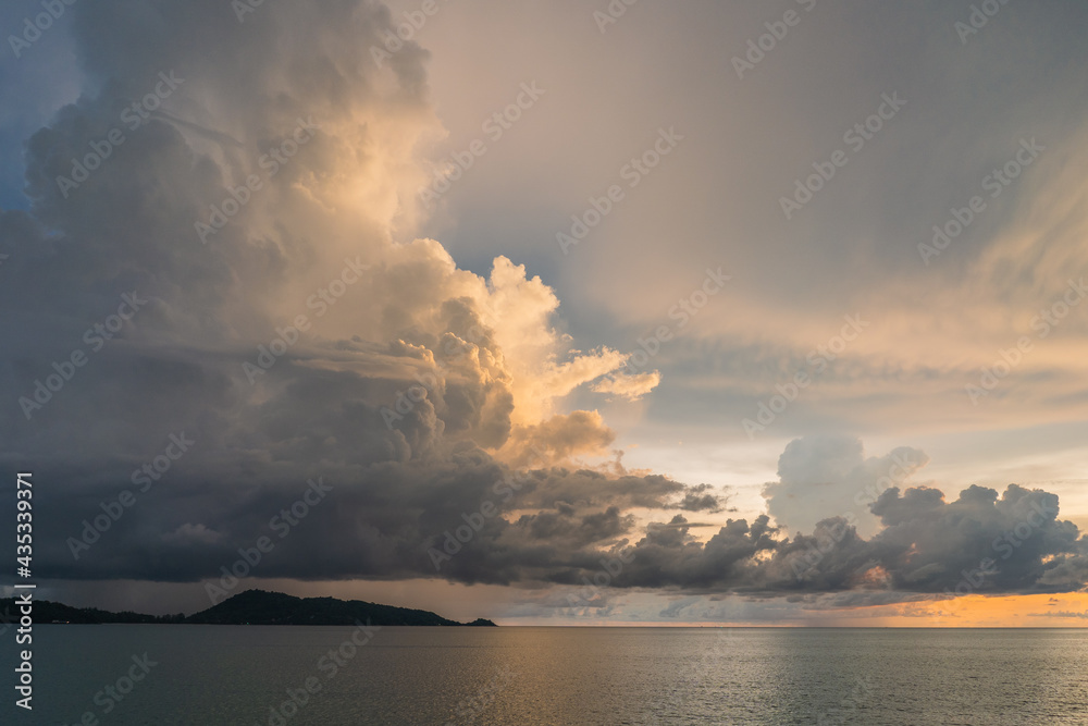 Grey blue sky with a big cloud coating with orange sunset light and sea