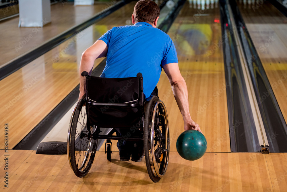 Young disabled man in wheelchair playing bowling in the club Young disabled man in wheelchair playing bowling in the club