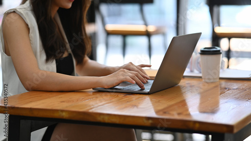 Cropped shot of businesswoman sitting in coffee shop and working with laptop computer on wooden table.