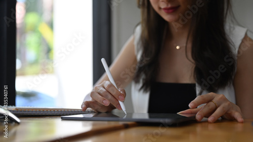 Cropped shot of young businesswoman using stylus pen writing on digital table while sitting in cafe.