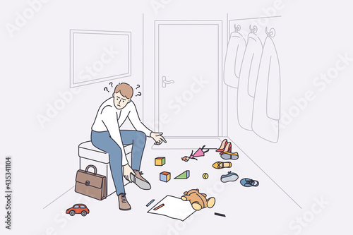 Anger and irritation concept. Young stressed man father cartoon character sitting at home feeling furious with child toys on floor putting off shoes vector illustration 