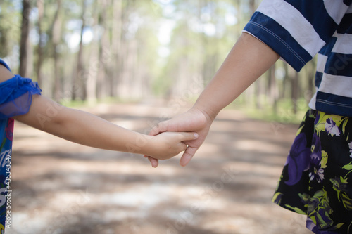 Two sweet little sisters walking in park. They are holding for the hands