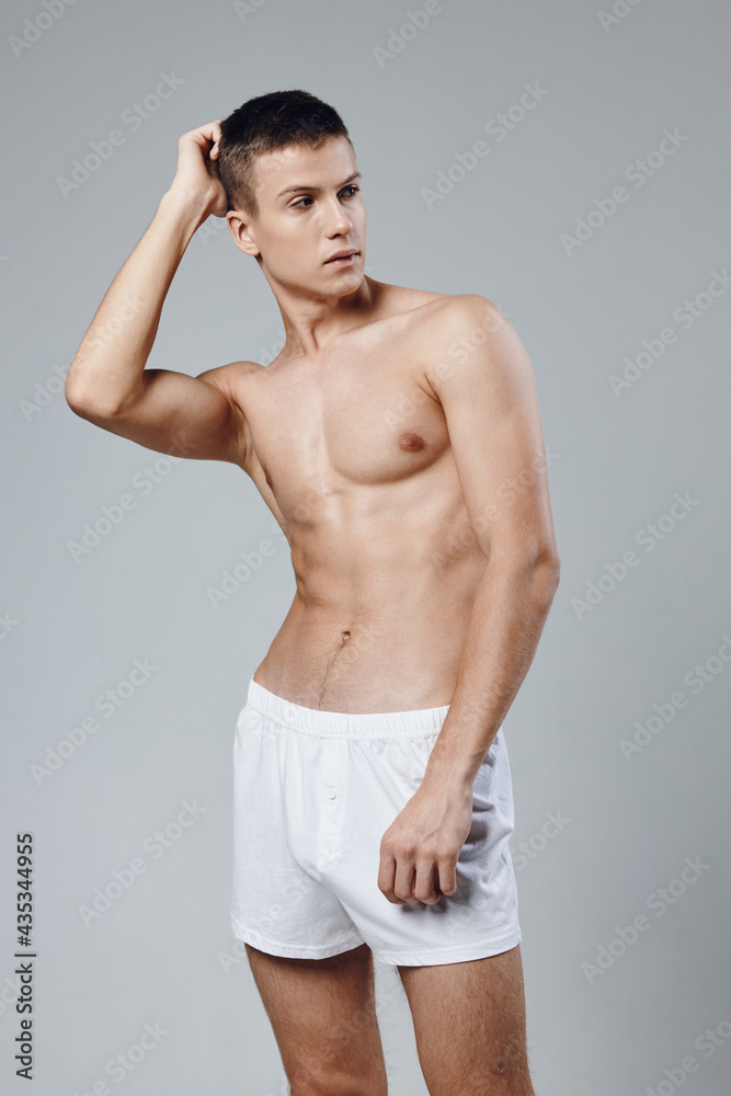Fototapeta premium athlete with a pumped-up torso holds his hand near his face and cubes on his stomach gray background 