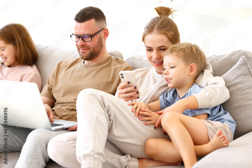 Young family addicted with gadgets relaxing on sofa at home