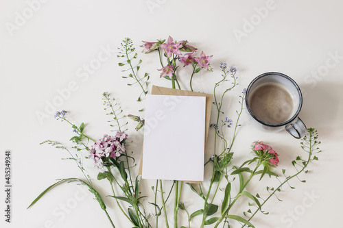 Fototapeta Naklejka Na Ścianę i Meble -  Summer greeting card, invitation mockup. Garden and wild meadow flowers. Floral banner and cup of coffee. Shepherd's purse, dianthus and aquilegia plants isolated on white table background. Flat lay.