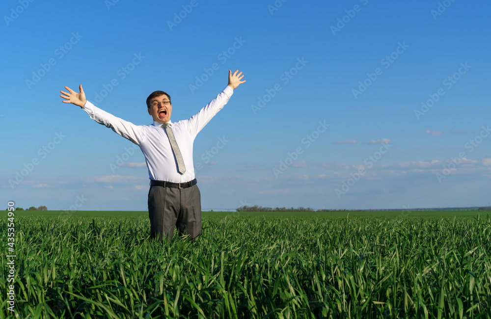 businessman poses in a field, he looks into the distance and rests, green grass and blue sky as background businessman poses in a field, he looks into the distance and rests, green grass and blue sky as background