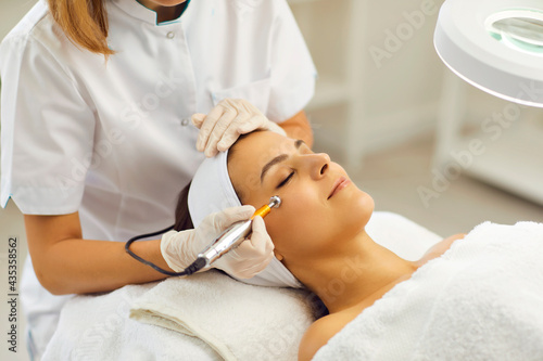 Beautician using electric mesotherapy device to decrease wrinkles on customer's face