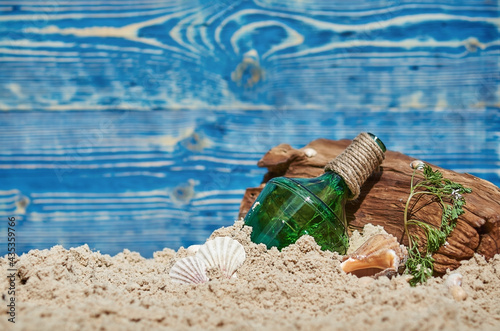 a green bottle with a rope is buried in the sand near a wooden snag on a blue wooden background