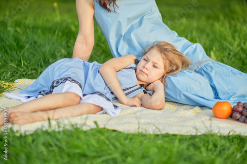 little girl resting on her mother's lap, summer warm day in the park. Happy family resting together. Happiness and harmony in family life.